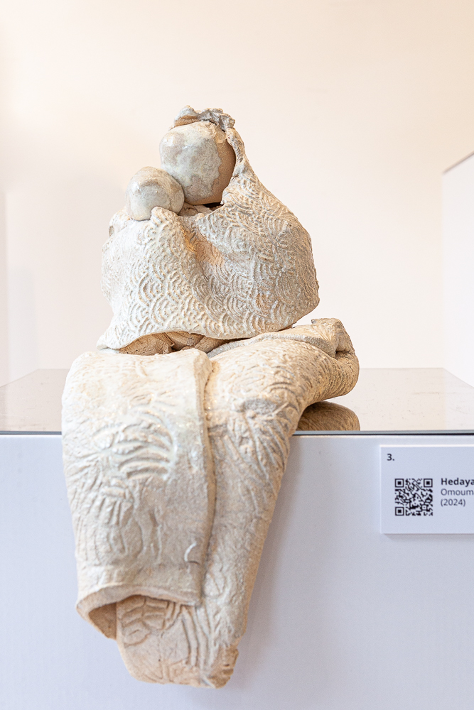 Close-up of a pale ceramic mother and child sculpture titled Omouma