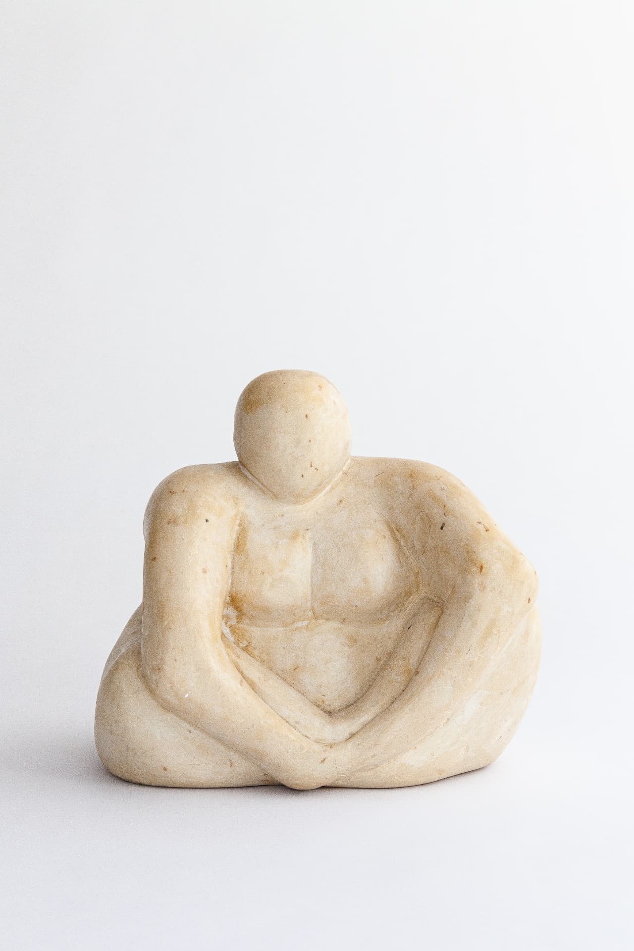 Seated pale stone figure with folded arms resting on crossed legs