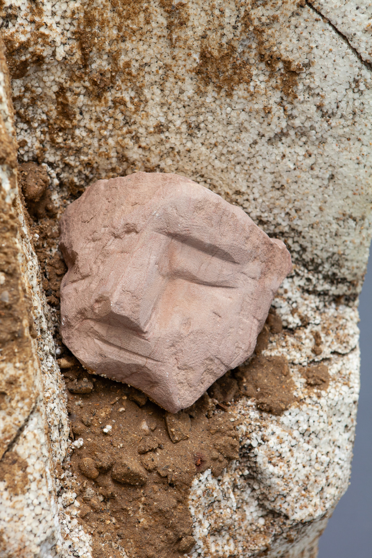 Close-up of a pink terracotta face fragment pressed into a sandy surface