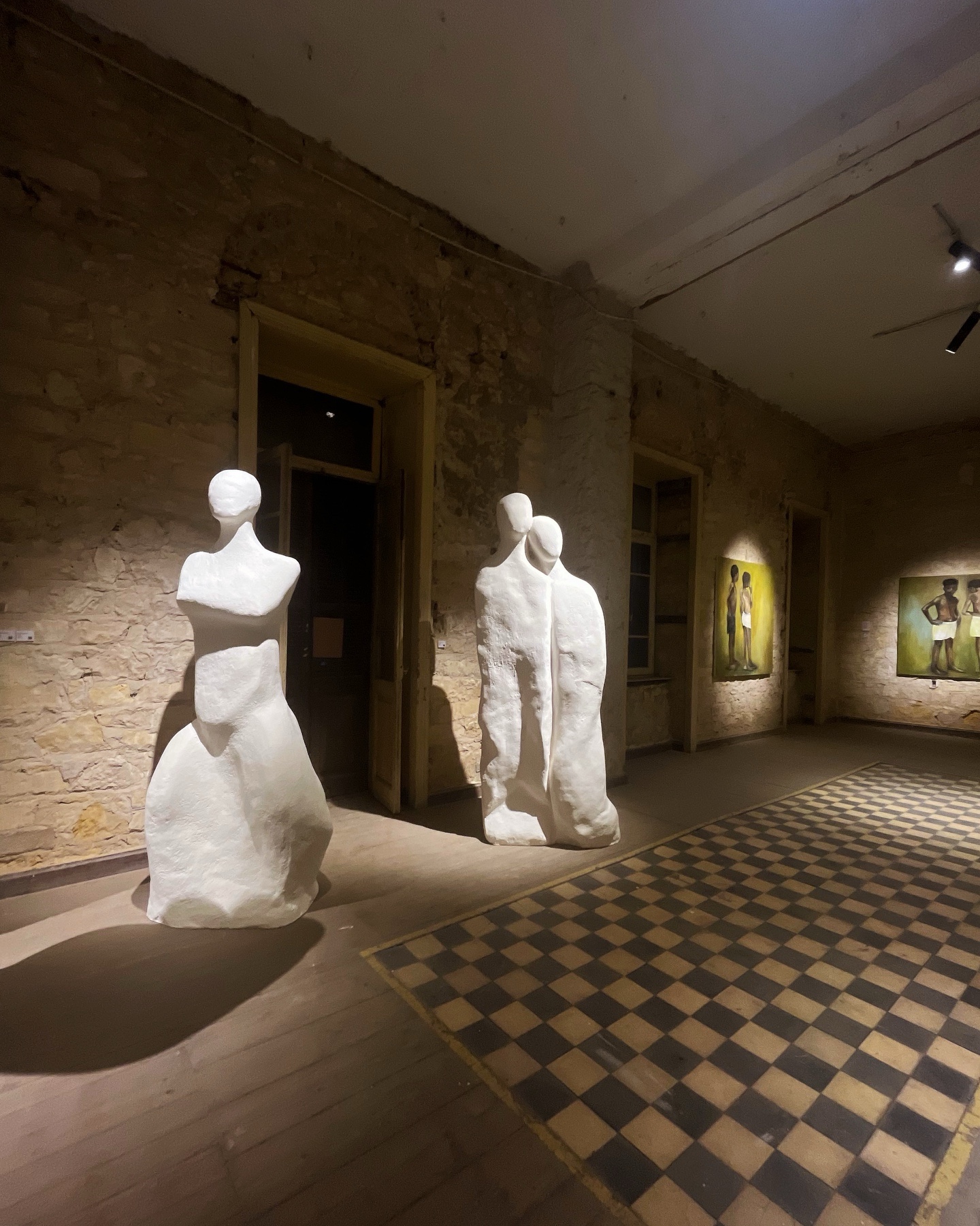 Installation view of large white plaster sculptures in a stone-walled gallery