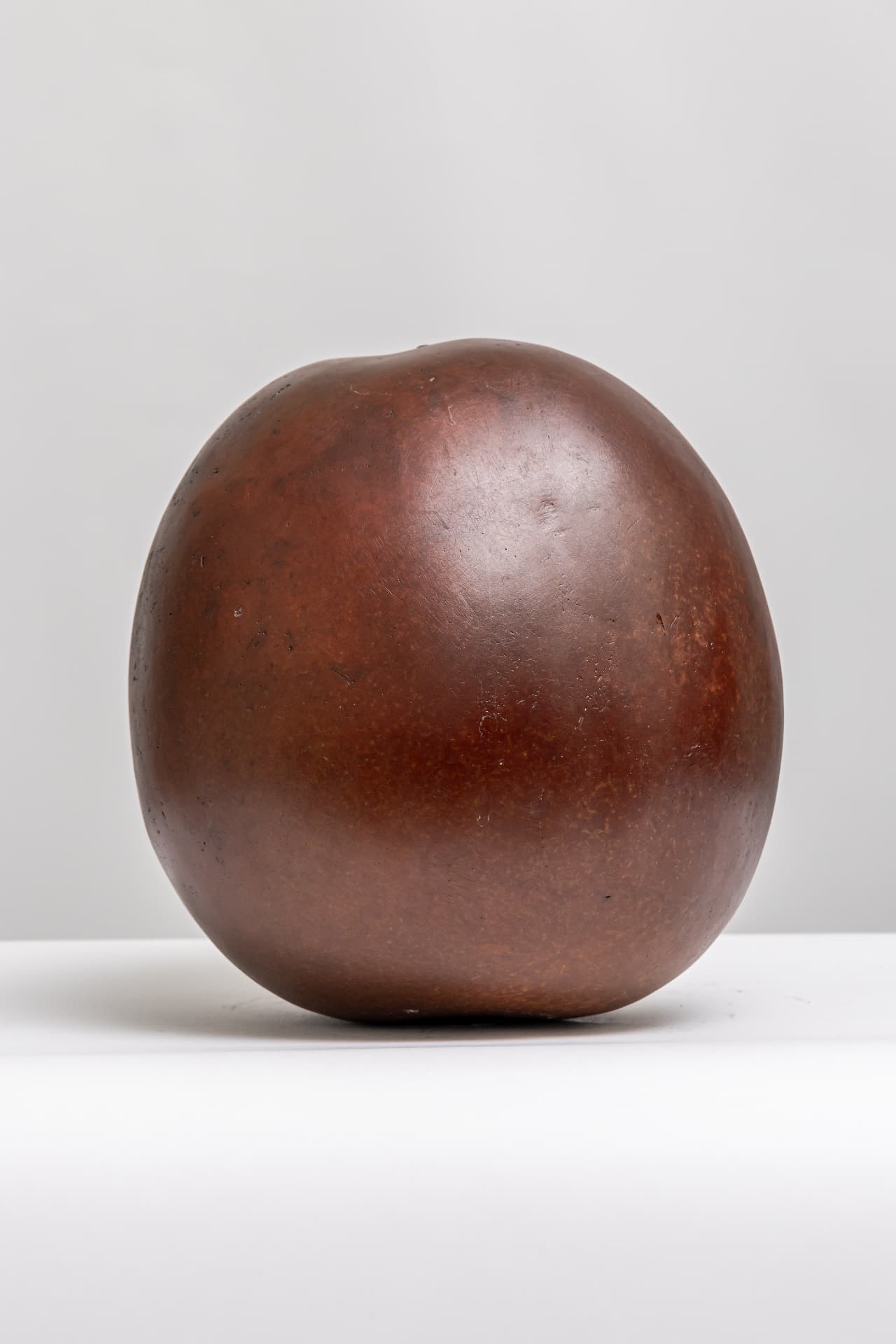 Bateekha I, bronze watermelon form, seated on a white surface