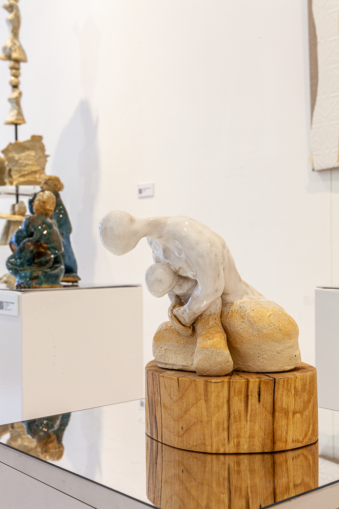 Close-up of a white glazed ceramic figure bent forward on a wooden base